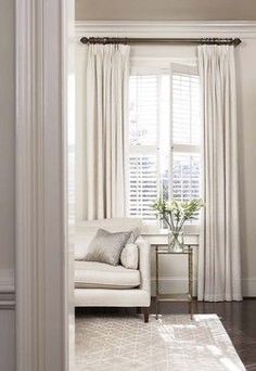 a white chair sitting in front of a window next to a vase filled with flowers