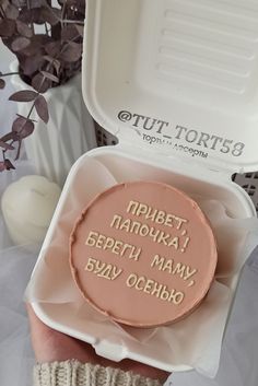 a person holding up a pink cake in a white box with writing on the inside