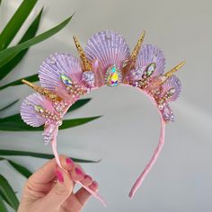 a hand holding up a pink headband with flowers on it and gold trimmings