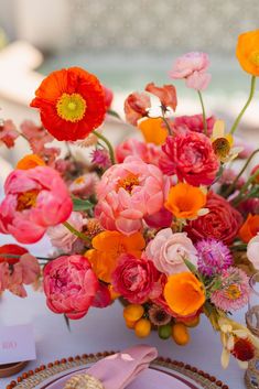 an arrangement of flowers in a vase on a table with plates and utensils