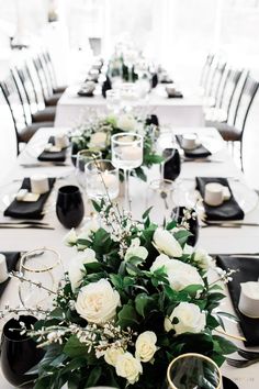 the table is set with black and white plates, silverware, and flower centerpieces