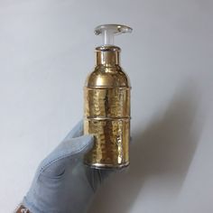 a hand in blue gloves holding a gold colored soap dispenser