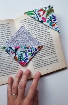 an open book with some fabric on top of it and a person's hand next to it