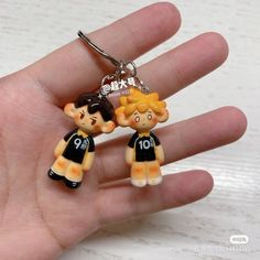 two small figurines are hanging from a keychain in someone's hand