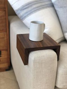 a wooden table with a white cup on it sitting on top of a couch next to pillows