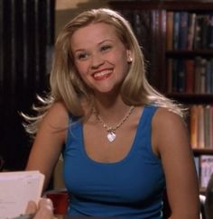 a woman sitting at a table with a book in her hand and smiling for the camera