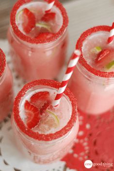 four glasses filled with pink liquid and strawberries on top of a white doily