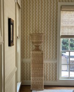 a tall wicker vase sitting in the corner of a room next to a window