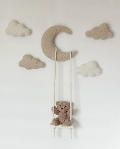 a teddy bear sitting on a swing in the shape of a crescent and clouds hanging from it's sides