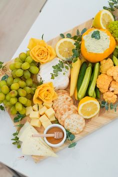 a wooden cutting board topped with lots of different types of cheeses and vegetables next to grapes