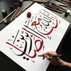 someone is doing calligraphy on a sheet of paper with colored pencils next to it