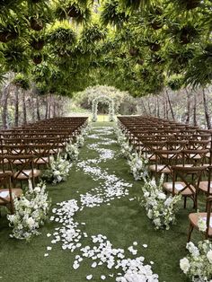 an outdoor ceremony with rows of chairs and white flowers on the aisle, surrounded by greenery