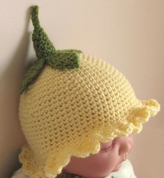 a crocheted lemon hat on top of a doll's head, against a wall