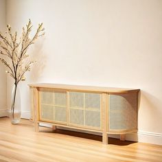 a wooden cabinet sitting on top of a hard wood floor next to a vase filled with flowers