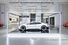 a white sports car in a showroom with its reflection on the floor and other cars behind it