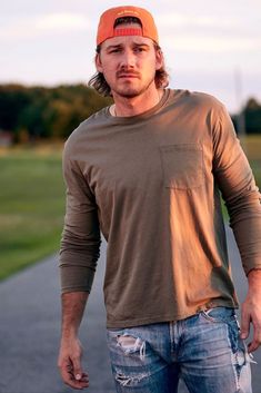 a man with a baseball cap is standing on the street and holding his skateboard