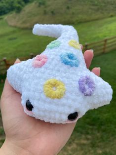 a hand holding a small white crocheted animal with flowers on it's face