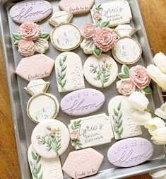 some cookies are on a tray with flowers and name tags in them for wedding favors