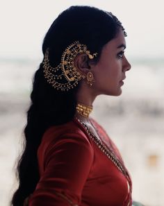 a woman in a red dress with gold jewelry on her neck and long hair is looking off into the distance