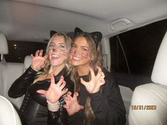 two women sitting in the back seat of a car making peace signs with their hands