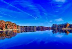 a lake surrounded by lots of trees and blue skies with clouds in the sky above it