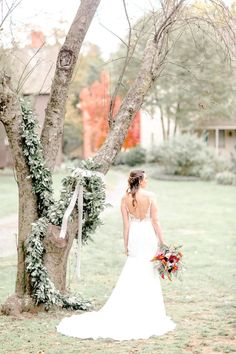 a bride standing in front of a tree with flowers and greenery on it's back