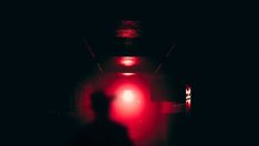 a person standing in front of a red light at the end of a dark hallway