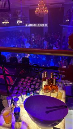 a table topped with lots of bottles and glasses next to a bowl filled with liquid