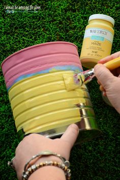 a person holding a paintbrush next to a bucket on the grass with other items in it