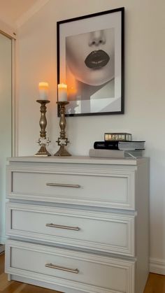 a white dresser with two candles on top and a framed photo above it in a bedroom