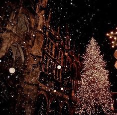 a large christmas tree is lit up in front of a church at night with snow falling on the ground