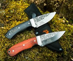 two knives sitting on top of moss covered ground