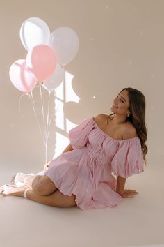 a woman in a pink dress sitting on the floor with balloons and smiling at her