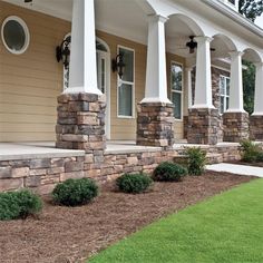 front porch with stone pillars and landscaping in the foreground, grass on the ground