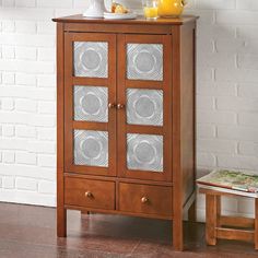 a wooden cabinet with glass doors next to a white brick wall and small side table