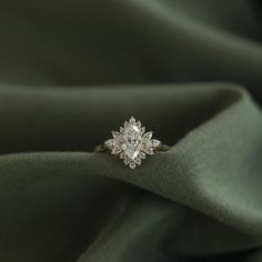 an engagement ring on top of a green satin material, with the center diamond surrounded by smaller diamonds