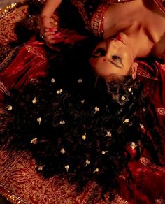 a woman laying on top of a red and gold cloth covered floor next to a stuffed animal