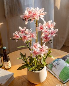 pink flowers sit in a white vase on a table next to a book and beer