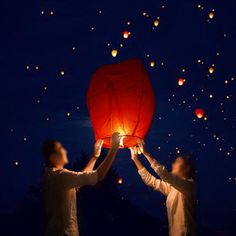 two people holding up a red lantern in the air at night with many lights on it