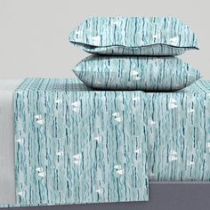 two pillows are stacked on top of each other in front of a bed with blue and white sheets