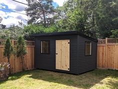 a small black shed sitting in the middle of a yard next to a wooden fence