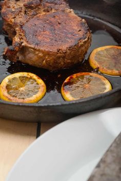 steak with lemons and sauce in a skillet on a wooden table, closeup