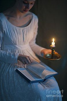 a woman in white dress holding an open book with a lit candle on top of it