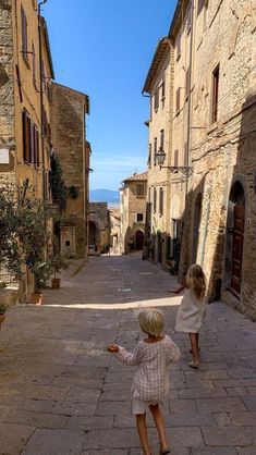 two young children playing with a kite in an alleyway between old stone buildings on a sunny day