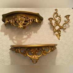 two antique brass shelf brackets with ornate designs on the top, and one is gold