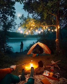 two people are camping in the woods at night with lights strung from trees and tent