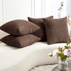 three pillows stacked on top of each other in front of a vase with pink flowers