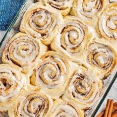 cinnamon rolls in a casserole dish with cinnamon sticks next to it on a table