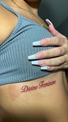 a woman's chest with the words divine feminine tattooed on her left arm and shoulder