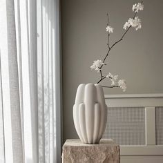 a white vase with flowers in it sitting on a stone block next to a window